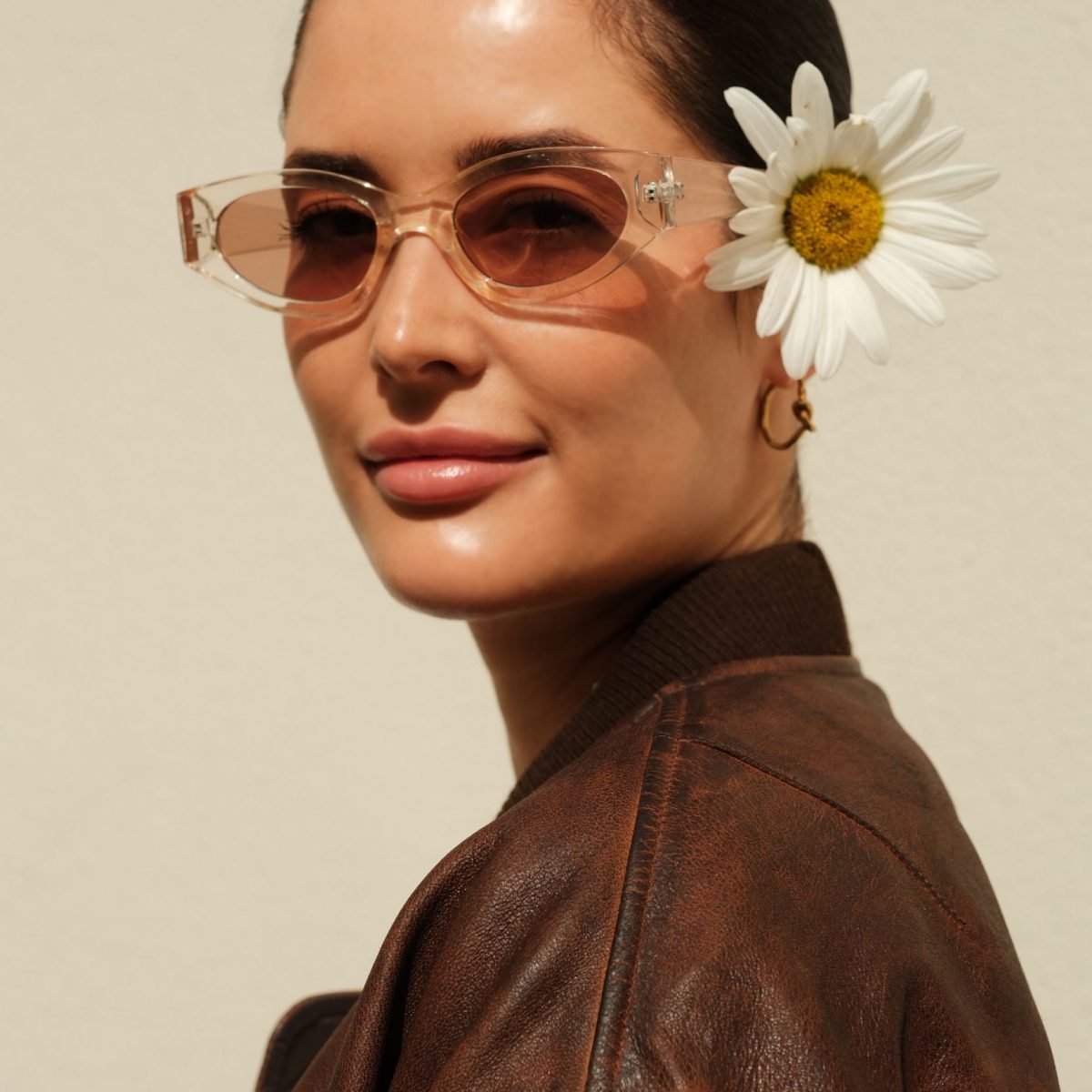 Fashion blogger Alina Barchet is posing for a fashion photo shooting in Paris. Alina Barchet styled sunglasses with a clear frame in the style of Bottega Veneta with small golden Celine knot hoop earrings and a brown leather bomber jacket in used optic from Mango.